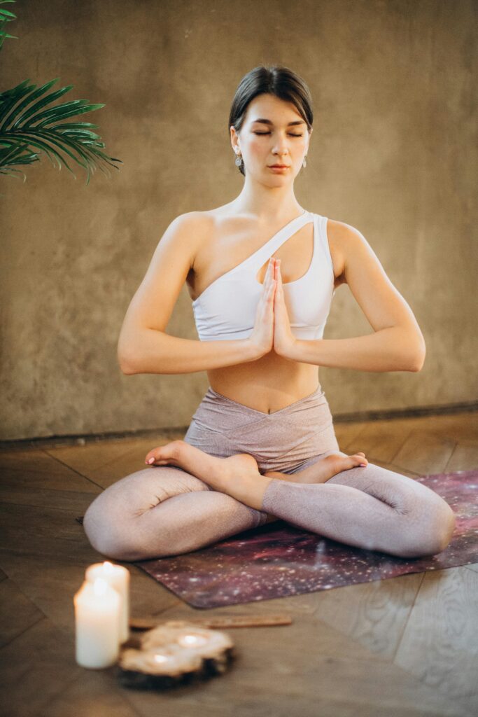 A woman meditating in a lotus pose with candles in a tranquil indoor setting.