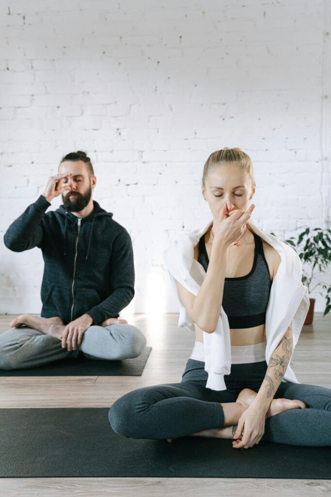 Two people meditating indoors, focusing on breathing exercises for relaxation and wellness.